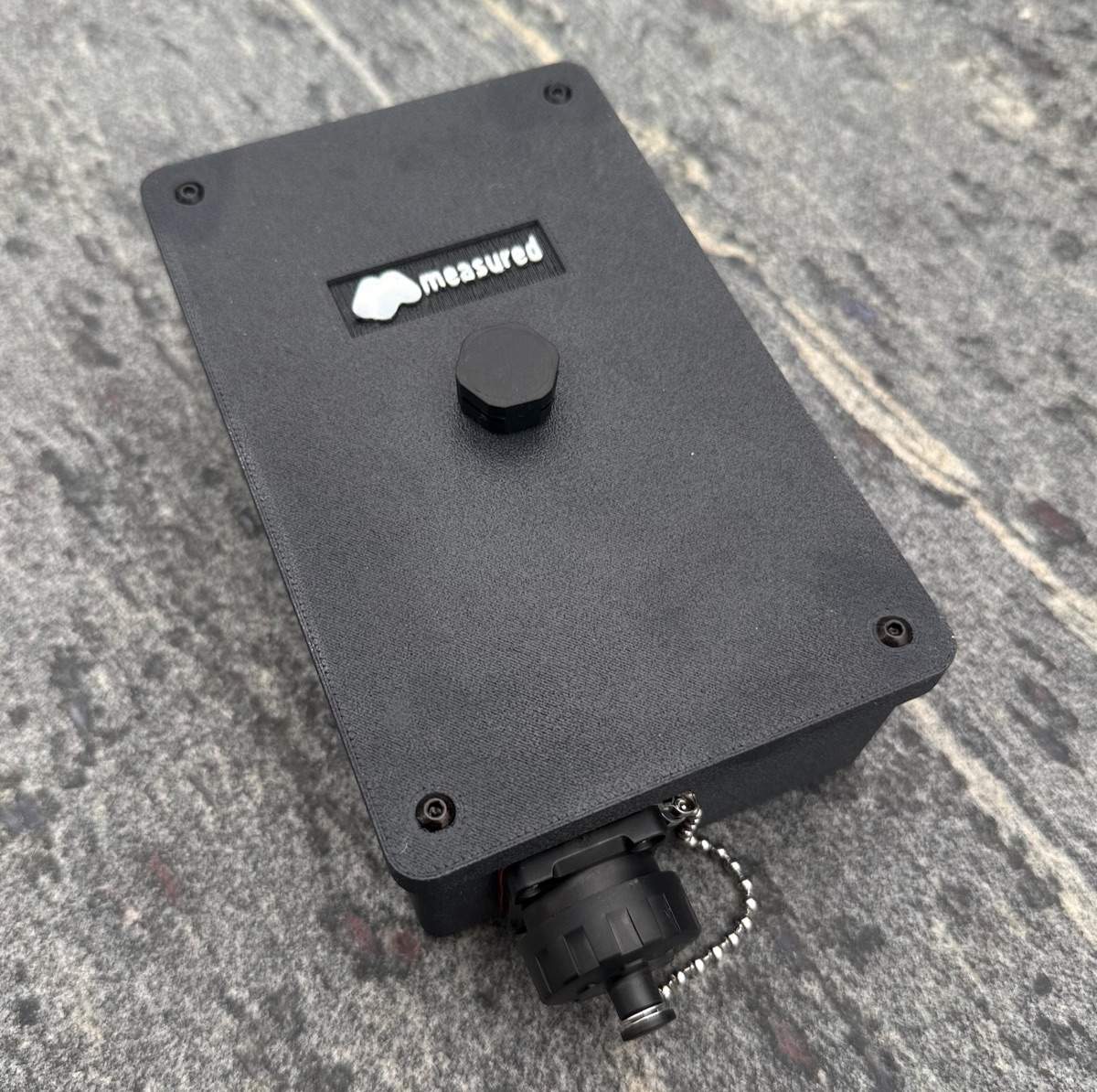 Black 3D-printed Measured enclosure with a sealed circular connector, resting on a granite surface